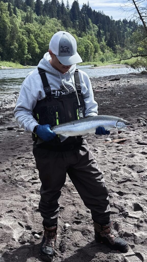 A fisherman holding a steelhead on the riverbank. 